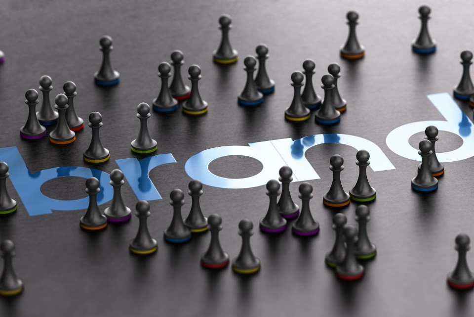 Chess pawns with colorful bases scattered on a surface, partially covering the word "brand"