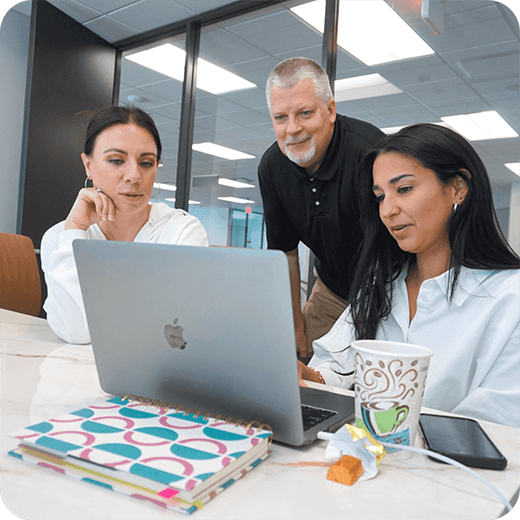 NLT marketing team collaborating around a laptop during a brand strategy meeting at the office in Houston