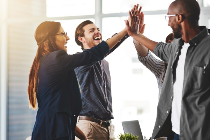 A group of brand strategists enthusiastically high-fiving in celebration during a team meeting
