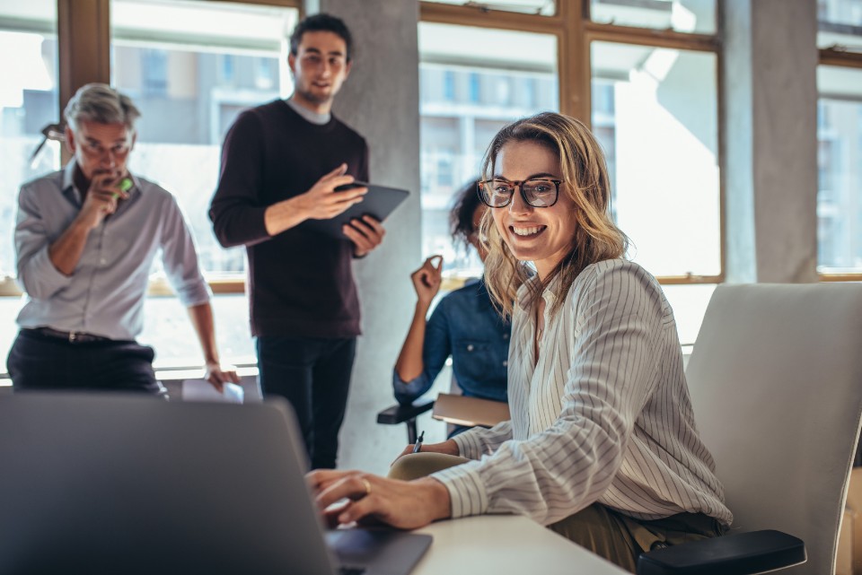 A cheerful team of brand strategists in an office setting, brainstorming ideas together while a team member works on her laptop